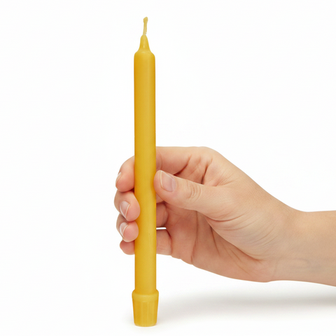 A hand holding a single yellow taper candle against a clean white background.