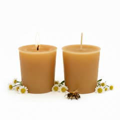 Two lit natural beeswax pillar candles in a warm golden-amber color, styled with chamomile flowers and a small honeybee on a clean white background.