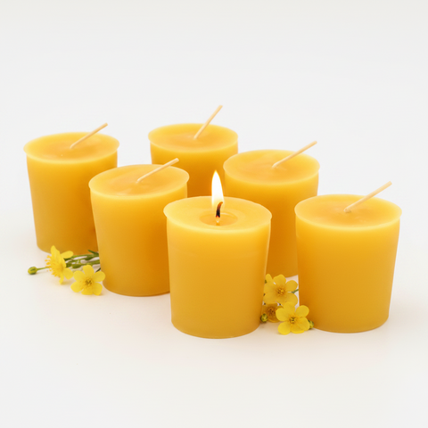 Six yellow votive candles on a white background with small yellow flowers; one wick is lit.