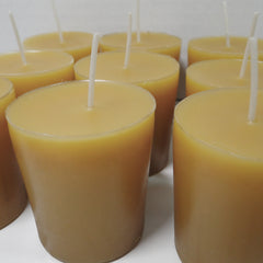A group of unlit beeswax candles, showing a warm tan wax color with white wicks, arranged closely together on a light surface.