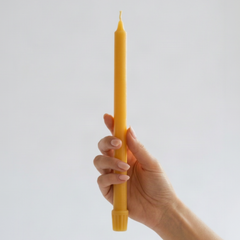 A hand holding a tall, slender yellow candle 