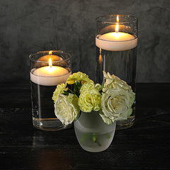 Glass candle holders with floating candles and flowers on a dark surface