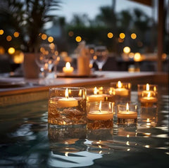 Candles in glasses on a reflective surface with blurred lights in the background