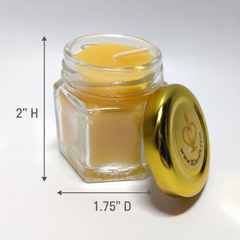 A small clear glass jar candle with yellow wax and a shiny gold lid placed beside it on a white background. Black measurement arrows and text indicate the jar is 2 inches high