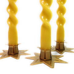 Three twisted yellow candles in gold candle holders on a white background