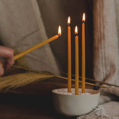 Candle being lit with a match in front of three already lit candles in a white container.