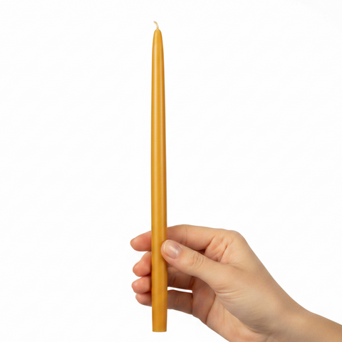 A single long, thin yellow taper candle standing vertically in hand a plain white background.