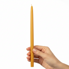 A single long, thin yellow taper candle standing vertically in hand a plain white background.