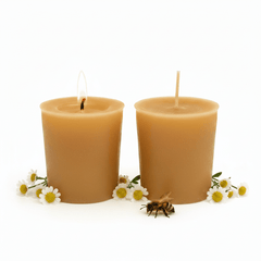 Two lit natural beeswax votive candles in a warm golden-amber color, styled with chamomile flowers and a small honeybee on a clean white background.