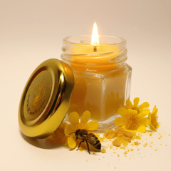 A small clear glass jar filled with yellow beeswax, shown with a shiny gold metal lid leaning against it on studio background